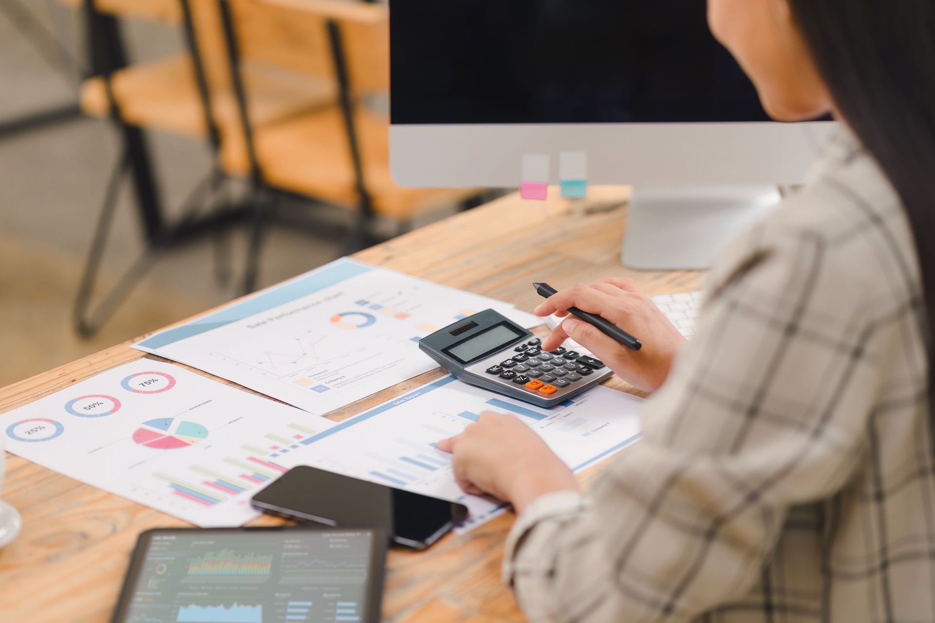 Businessperson calculating budget with calculator and analyzing financial charts and graphs on documents at a wooden desk.