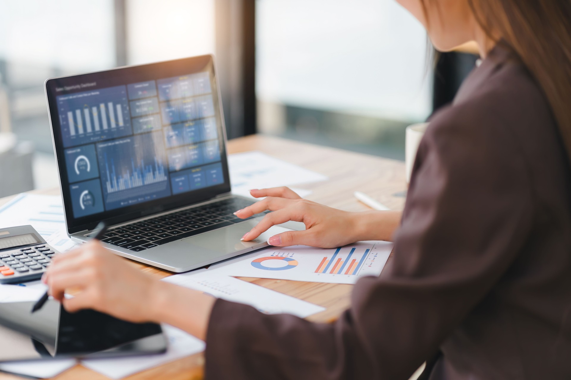 Profesional de negocios que trabaja en una computadora portátil con un panel de análisis, rodeado de informes financieros.